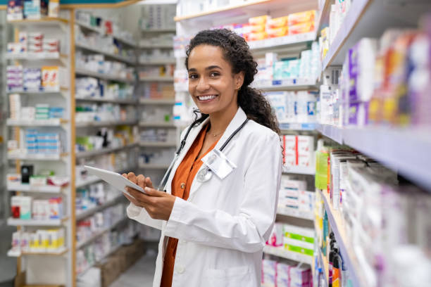 istockphoto-1248170454-612x612 Happy friendly multiethnic pharmacist doing inventory in a provided and modern pharmacy while looking at camera. Portrait of smiling young doctor woman working in drugstore with digital tablet. African smiling druggist working at hospital pharmacy.